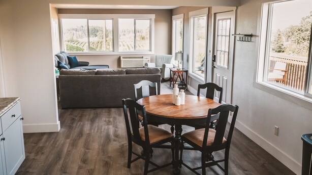 A dining area with a wooden table and chairs, a gray sofa, and large windows with a view of greenery. - Beautiful 2 bedroom home with amazing views (Gaston)