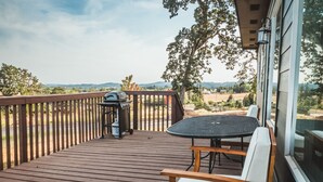A wooden deck with a table and chairs, a grill, and a view of the landscape. - Beautiful 2 bedroom home with amazing views (Gaston)