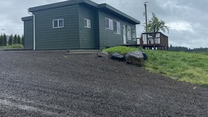 A two-story house with a dark exterior, a porch, and a gravel driveway. - Beautiful 2 bedroom home with amazing views (Gaston)