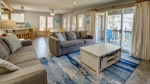 Un vaste espace de vie comprenant un ensemble de canapés, une table basse et une table à manger avec des chaises. Une porte-fenêtre coulissante donne accès à un espace extérieur.