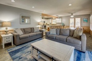 A modern living room with two grey sofas, a coffee table, and a dining area with wooden chairs.