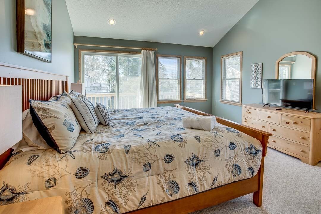 A bedroom with a large bed, a TV, a dresser, and a window with curtains.