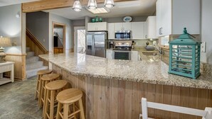 Une cuisine dotée d’un plan de travail en granit, de tabourets en bois, d’appareils électroménagers en acier inoxydable et d’une étagère de couleur turquoise.