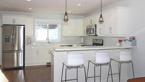 Cocina moderna con gabinetes blancos, electrodomésticos de acero inoxidable y una zona de bar con taburetes.