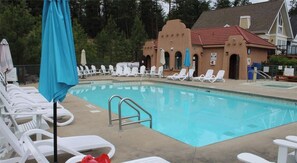 Une piscine entourée de chaises longues blanches et agrémentée d’un parasol bleu, le tout bordé par un bâtiment au toit rouge.