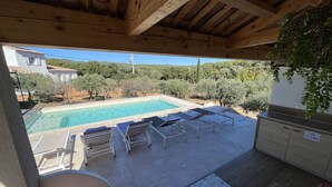 Ein überdachter Außenbereich mit Pool, Liegestühlen, einem Tisch und Blick auf die umliegende Landschaft.
