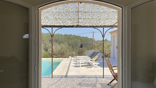 Ein Zimmer mit einer Schiebetür, die auf einen Poolbereich mit Liegestühlen und einer Pergola führt.