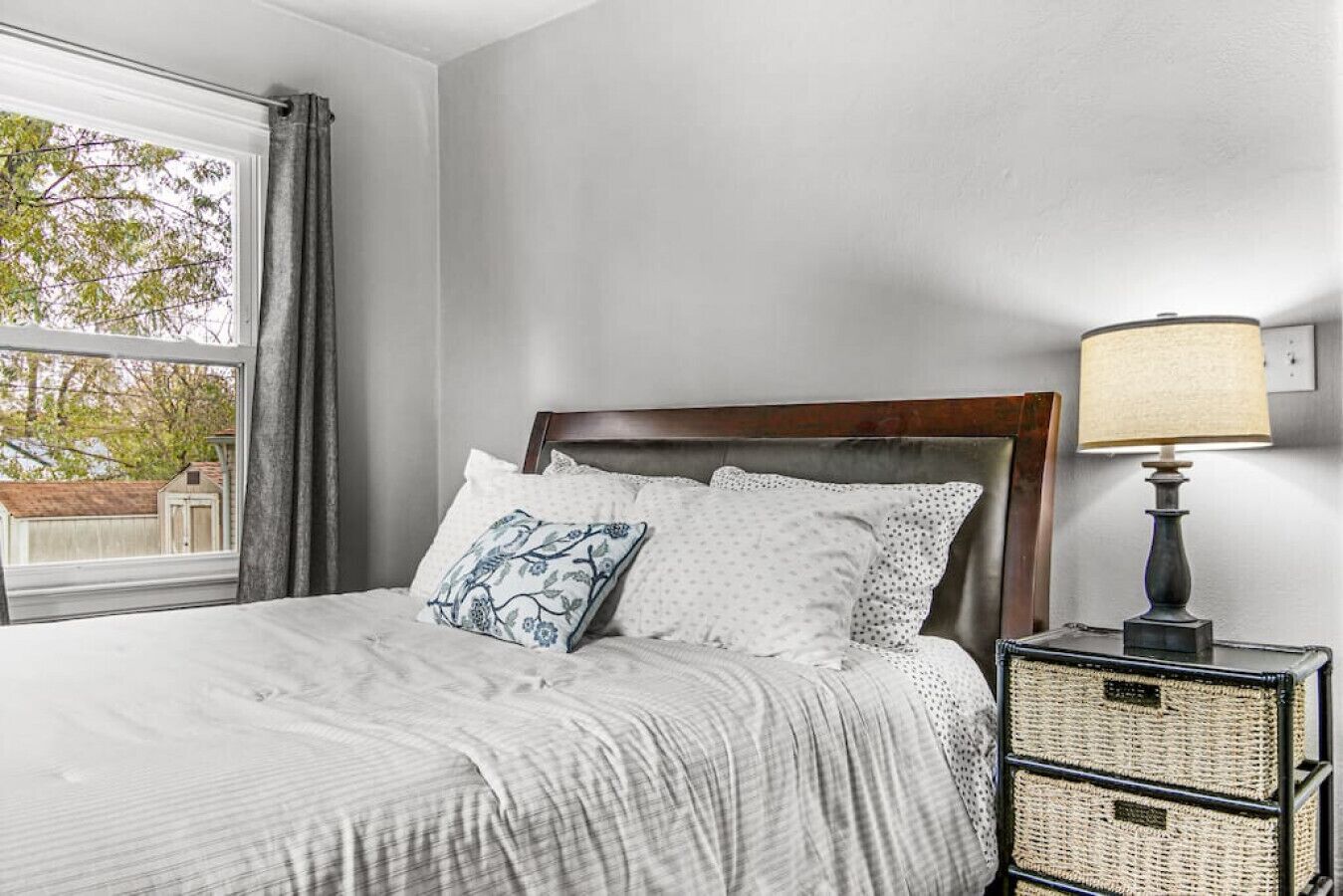 A bedroom with a bed, a nightstand, a lamp, and a window with curtains.
