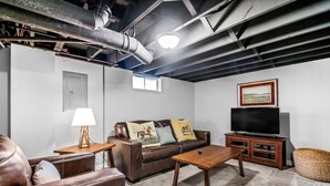 Ein Wohnzimmer mit braunem Ledersofa, einem Couchtisch aus Holz, einem Fernseher auf einem Holzständer und einer Lampe auf einem Nachttisch aus Holz.