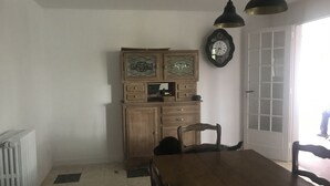 A dining area with a wooden table and chairs, a cabinet with decorative glass panels, a wall clock, and a radiator. - 10 minutes from Penly Ideal for seasonal workers, athletes and walkers (bailly en rivière)