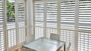 A sunlit room with a glass table and four white chairs, surrounded by white blinds. - Top Spot on Macrossan, Port Douglas 100m to Beach (Port Douglas)