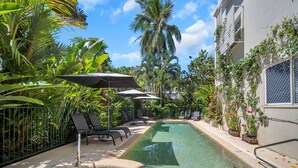 A pool area with lounge chairs and umbrellas, surrounded by tropical plants and a building with a window. - Top Spot on Macrossan, Port Douglas 100m to Beach (Port Douglas)