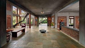 A spacious indoor area with a central seating area, brick walls, and large windows allowing natural light. - amã Stays & Trails The Mango House, Alibag (Alibag)