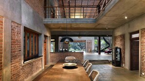 A spacious dining area with a long wooden table, brick walls, and a mezzanine level. - amã Stays & Trails The Mango House, Alibag (Alibag)
