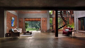 A spacious living area with a brick wall, a sofa, a red armchair, a coffee table, and a staircase leading to an outdoor area. - amã Stays & Trails The Mango House, Alibag (Alibag)