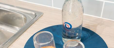 Un comptoir de cuisine avec un tapis bleu, une bouteille d’eau et deux verres posés sur des sous-verres en bois.