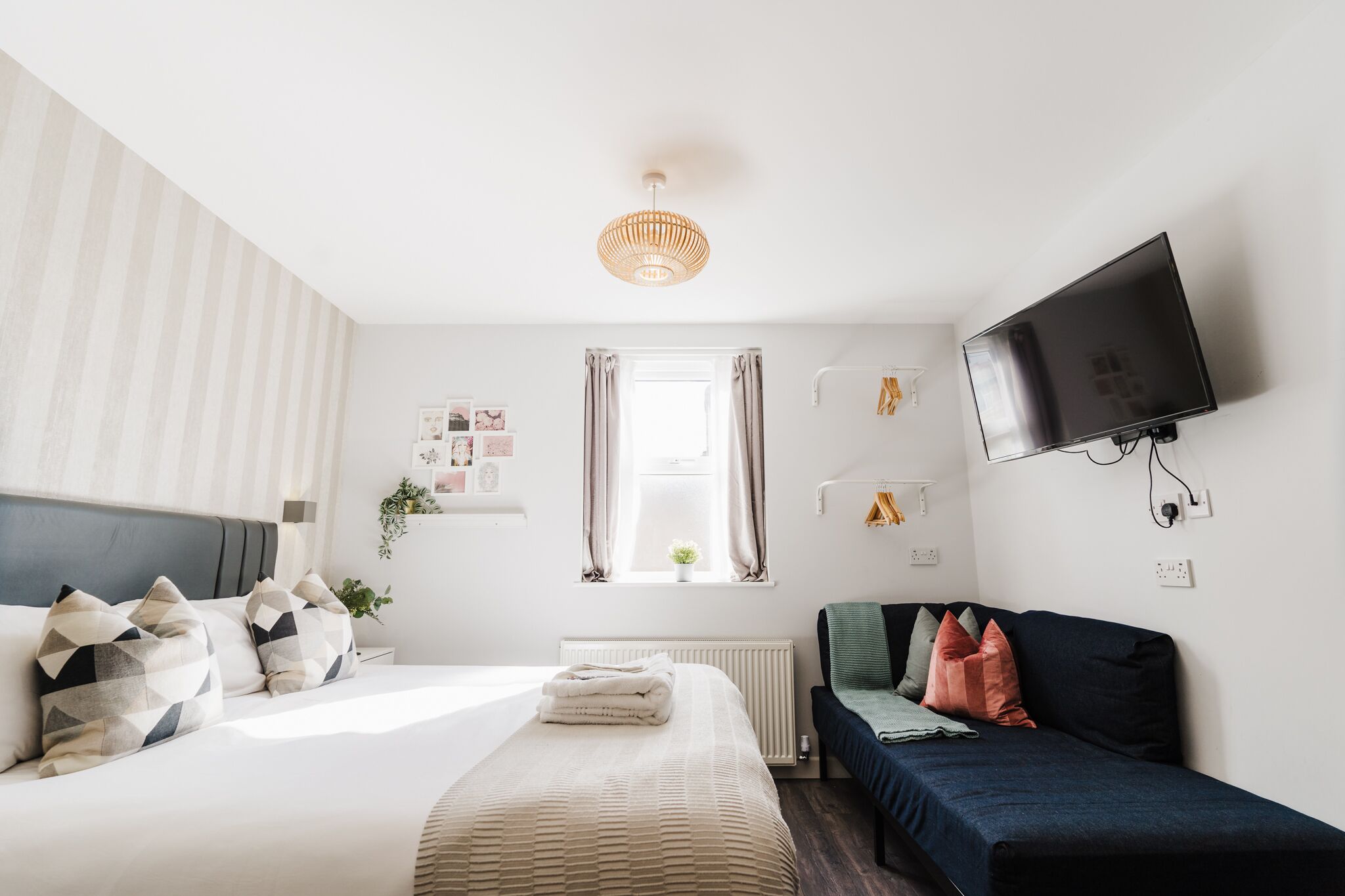 Un dormitorio moderno con cama, sofá, televisión y ventana con cortinas.