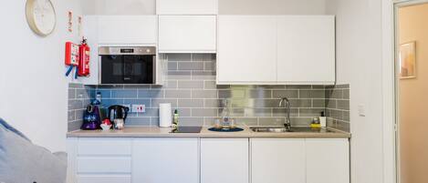 A compact kitchen with white cabinets, a microwave, a sink, and a coffee maker.