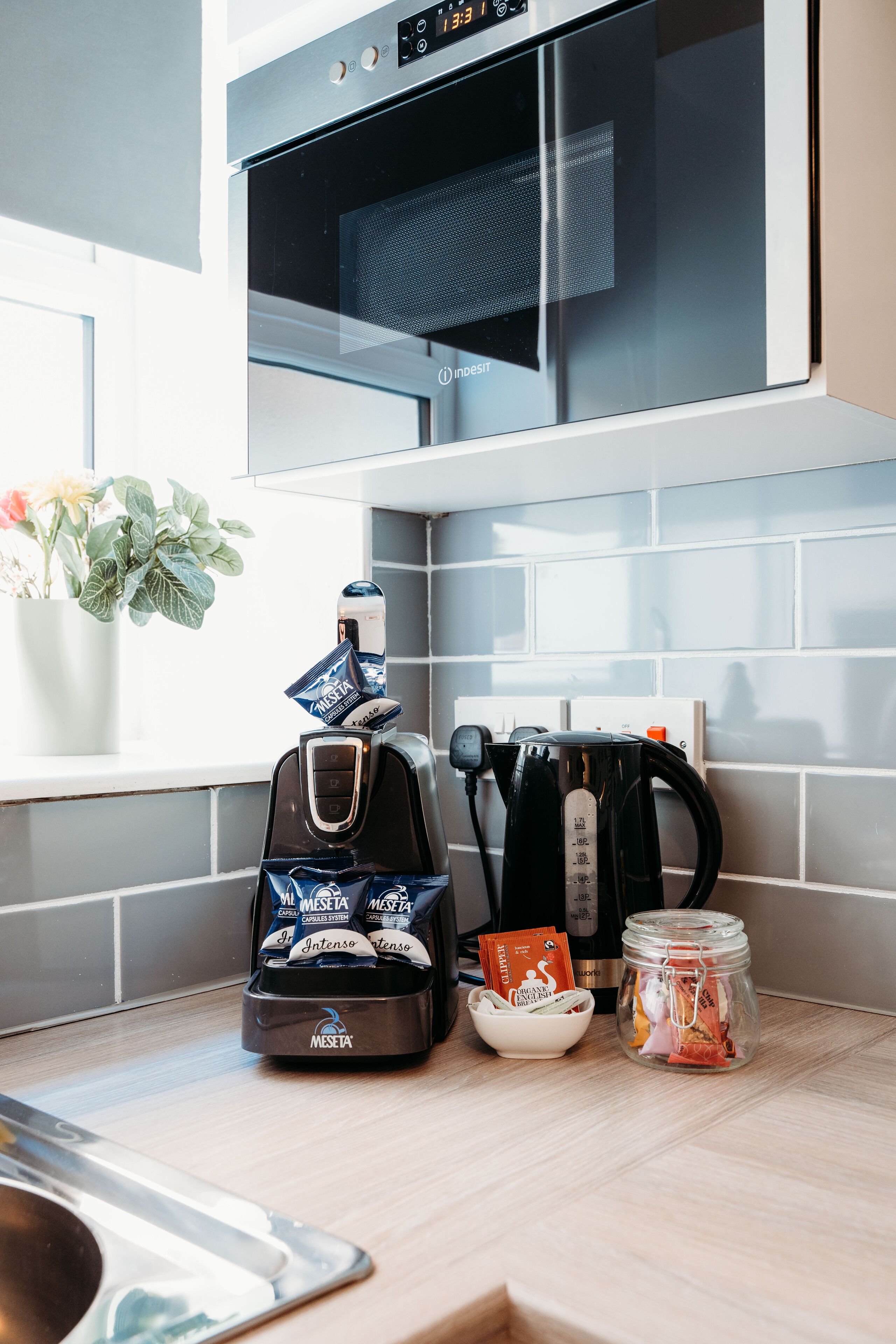 A kitchen with a coffee maker, a kettle, a jar, and a plant.