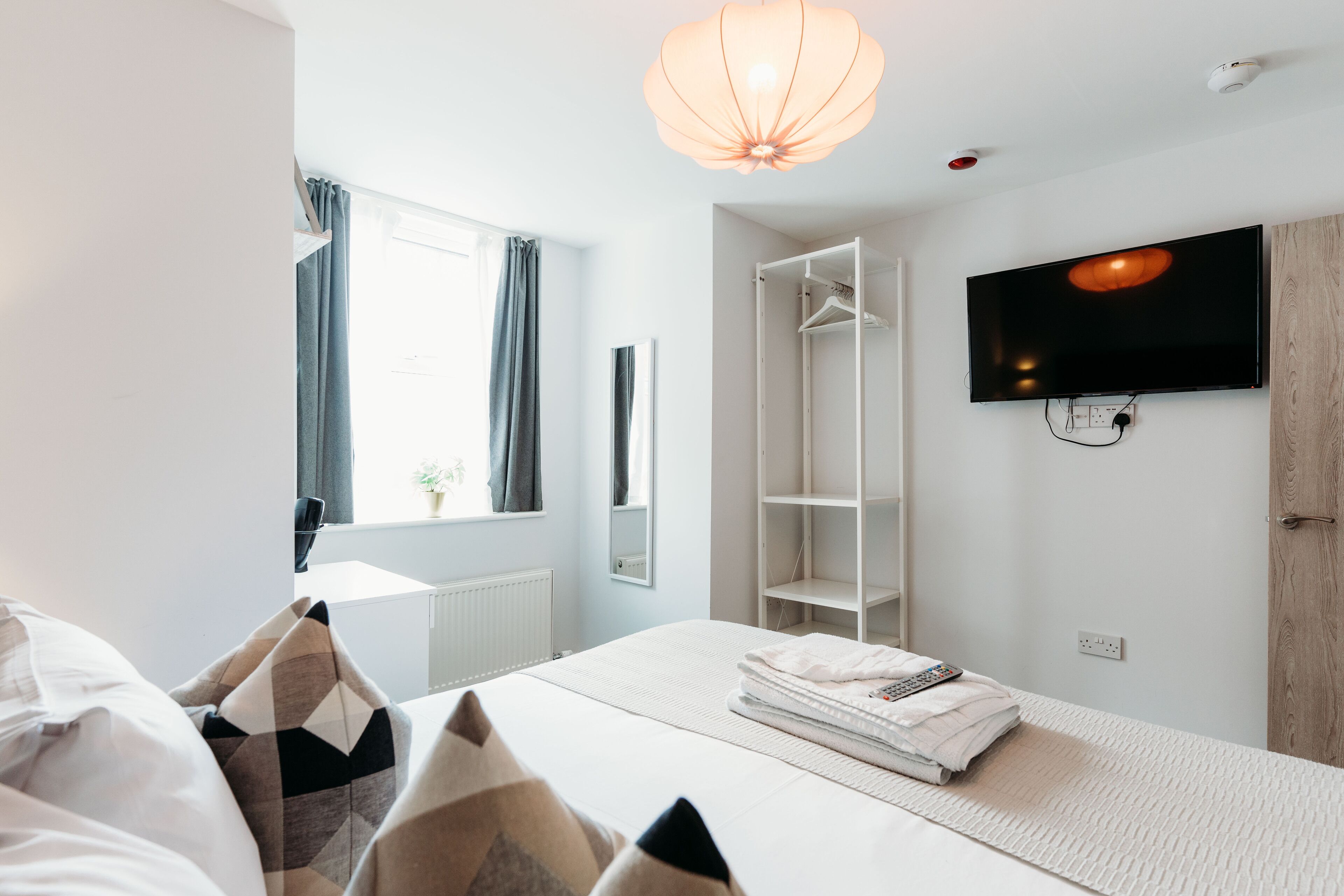 A modern bedroom with a bed, a TV, a wardrobe, and a window with curtains.