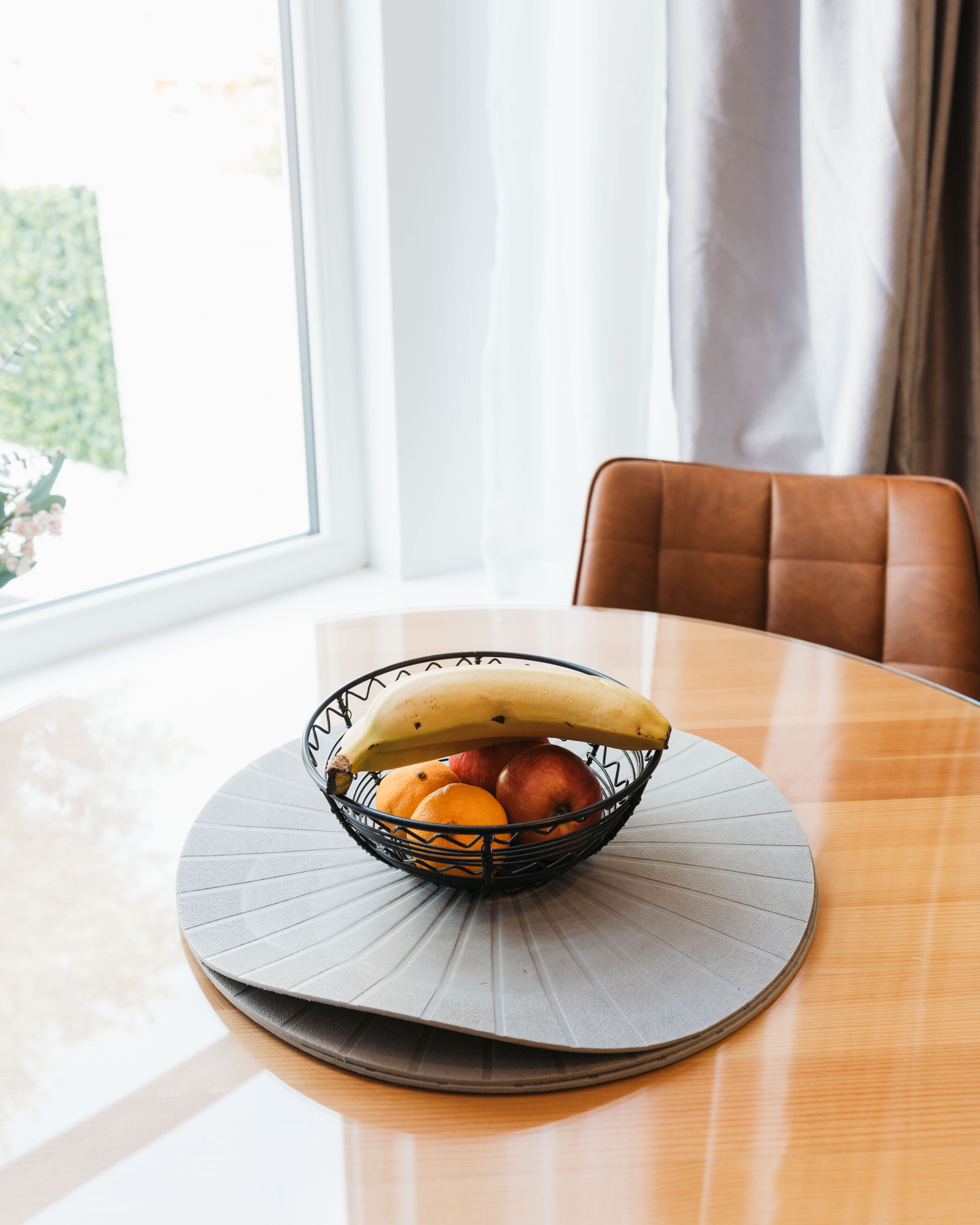 Un tavolo rotondo con un cesto di frutta intrecciato che contiene una banana, mele e arance.