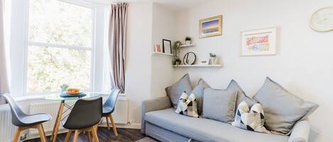 A modern living room with a grey sofa, two chairs, a glass table, and a window with curtains.