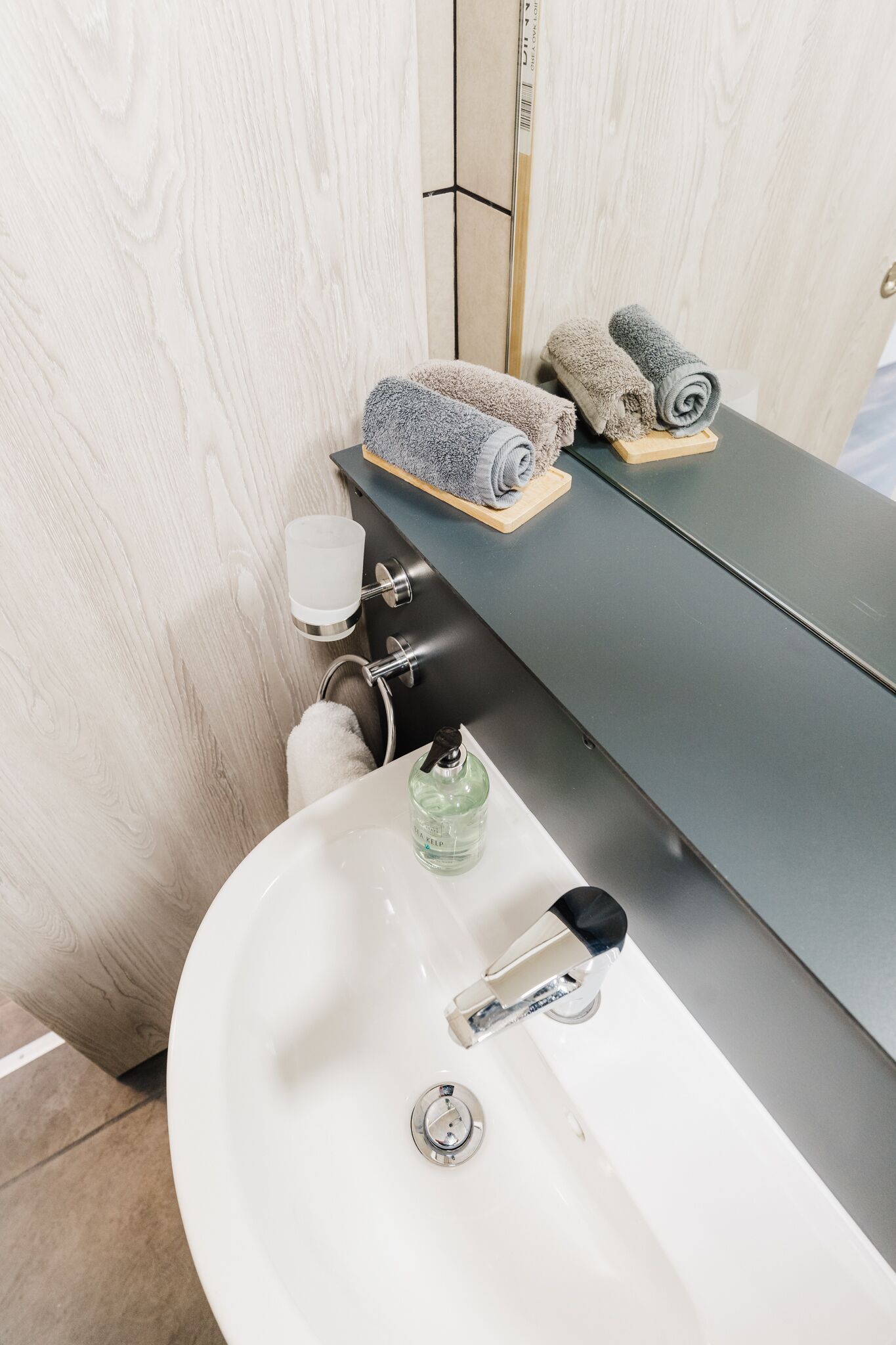 A bathroom with a white sink, a mirror, and two towels on a wooden shelf.