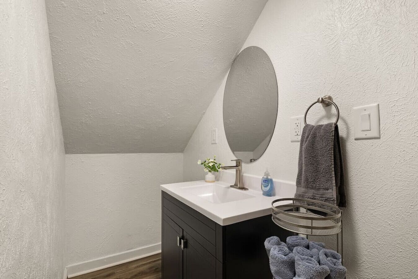 A bathroom with a white sink, dark cabinets, a mirror, a towel rack, and a small plant.