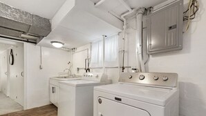 A laundry room with two white washing machines, a sink, and a window.