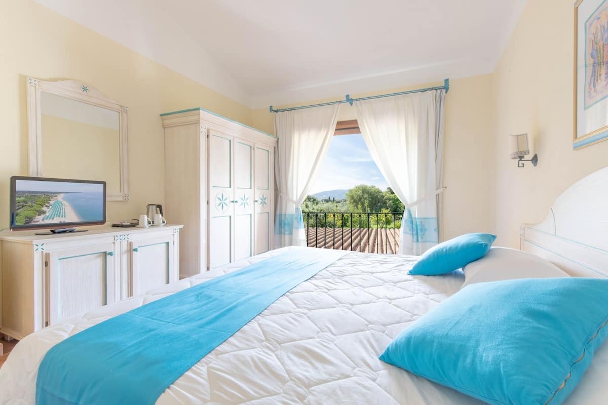 A bedroom with a bed, a television on a dresser, and a balcony with curtains.