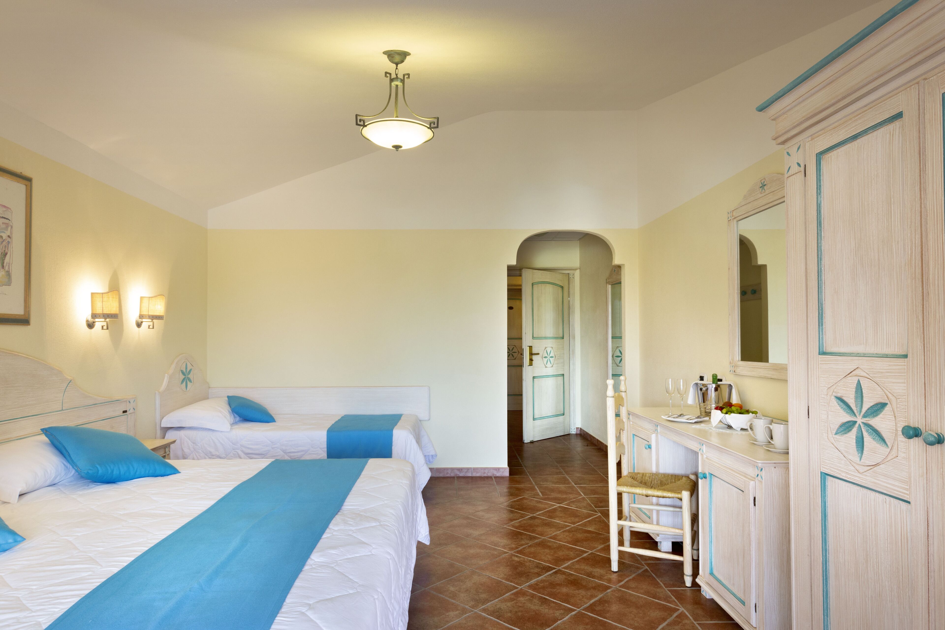 Una habitación de hotel con dos camas, un tocador con espejo y una puerta que da a otra habitación.
