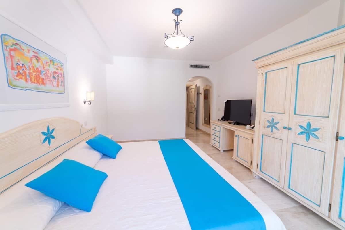 A bedroom with a bed, a desk, a television, and a wardrobe.