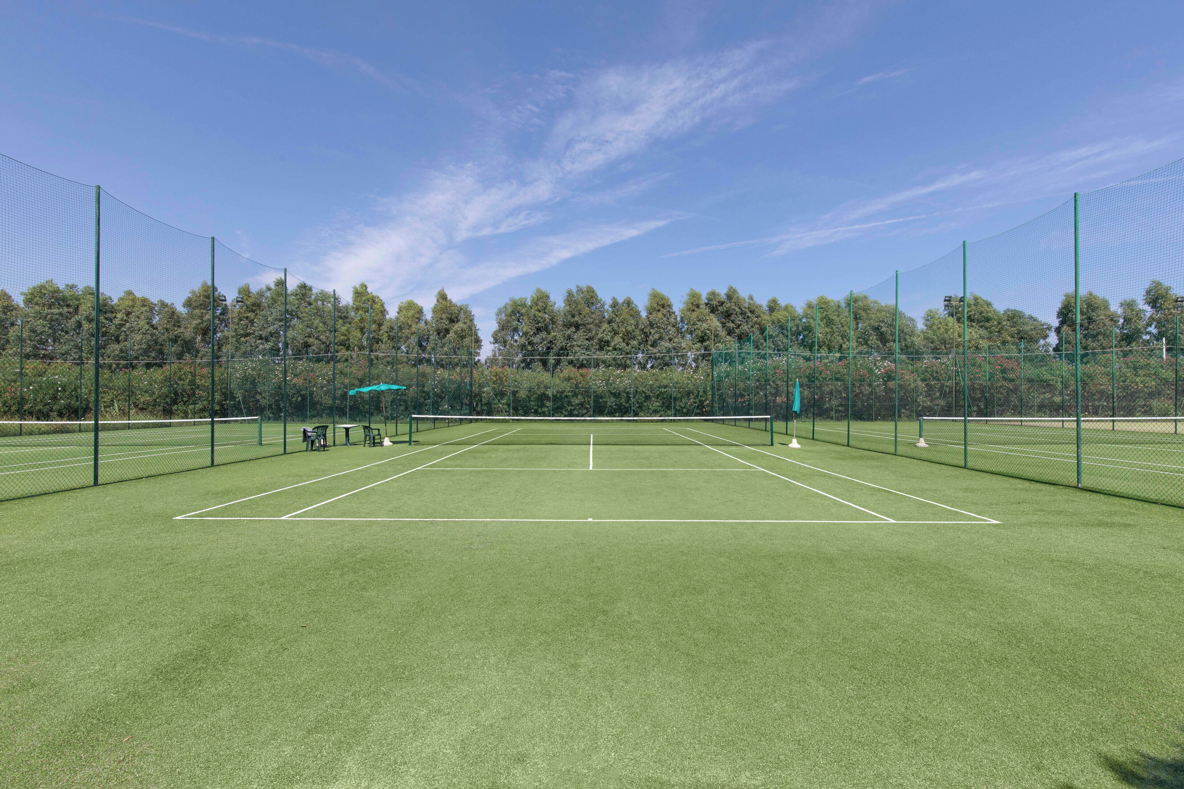 Un court de tennis avec un filet, entouré d’une clôture, et des arbres en arrière-plan.