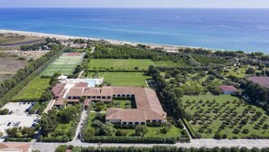 An aerial view of a coastal property with a large building, tennis courts, and a beach. - Sentido Orosei Beach (Orosei)