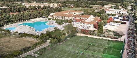 A resort with a large swimming pool, tennis courts, and a mountainous backdrop.
