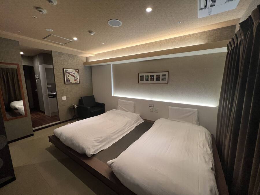 A hotel room with two beds, a small desk, a chair, a mirror, and a wall-mounted picture frame.