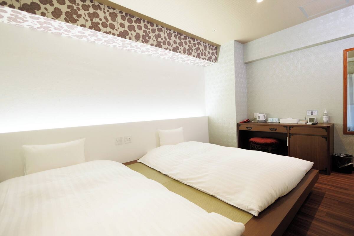 A hotel room with two beds, a desk, and a mirror.