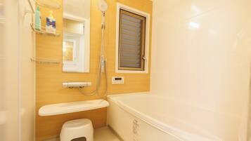 A bathroom with a bathtub, a shower, a toilet, and a small stool.