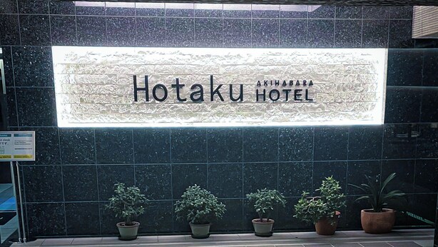En hotellskylt med namnet ”Hotaku Hotel” och fyra krukväxter framför.