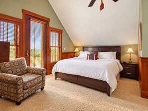 A bedroom with a large bed, two bedside tables, a chair, and a ceiling fan.
