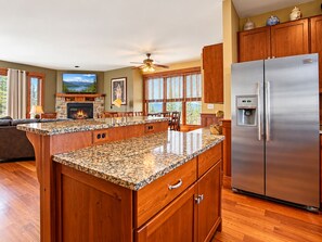 A kitchen with wooden cabinets, granite countertops, a stainless steel refrigerator, and a fireplace.