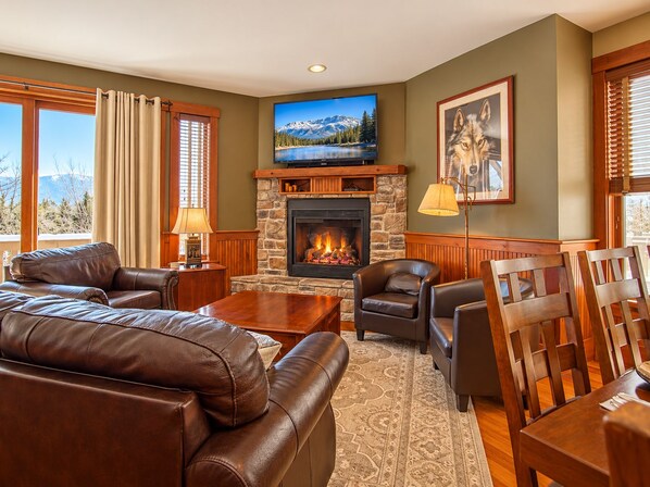 A living room with a stone fireplace, leather furniture, a television, and a large window with a mountain view.