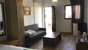 Una camera d'albergo moderna con divano, un tavolino, televisore e un'ampia finestra con tende.