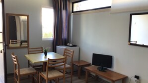 Una stanza con un tavolo da pranzo, quattro sedie, una televisione e una finestra con tende.