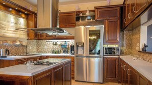 A modern kitchen with wooden cabinets, a stainless steel refrigerator, and a tiled backsplash. - Villa Napolia - Luxury Villa With Amazing Sea View (Zakynthos)