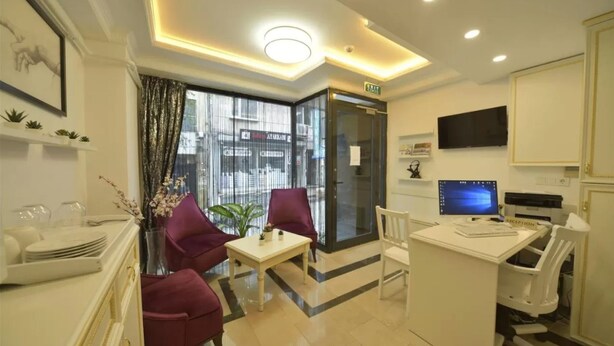 A hotel reception area with a reception desk, computer, seating area, and a large window with curtains. - Lika Hotel - Eco Double Room (Istanbul)