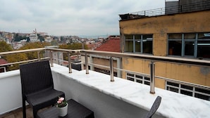 Ein Balkon mit zwei Korbstühlen und einem kleinen Tisch, mit Blick auf eine Stadtlandschaft mit Gebäuden und einer Moschee.