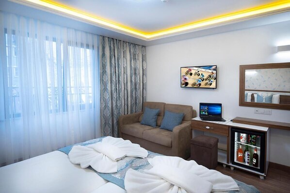 Une chambre d’hôtel équipée d’un lit, d’un canapé, d’un bureau avec un ordinateur portable, d’une télévision et d’un mini-bar.