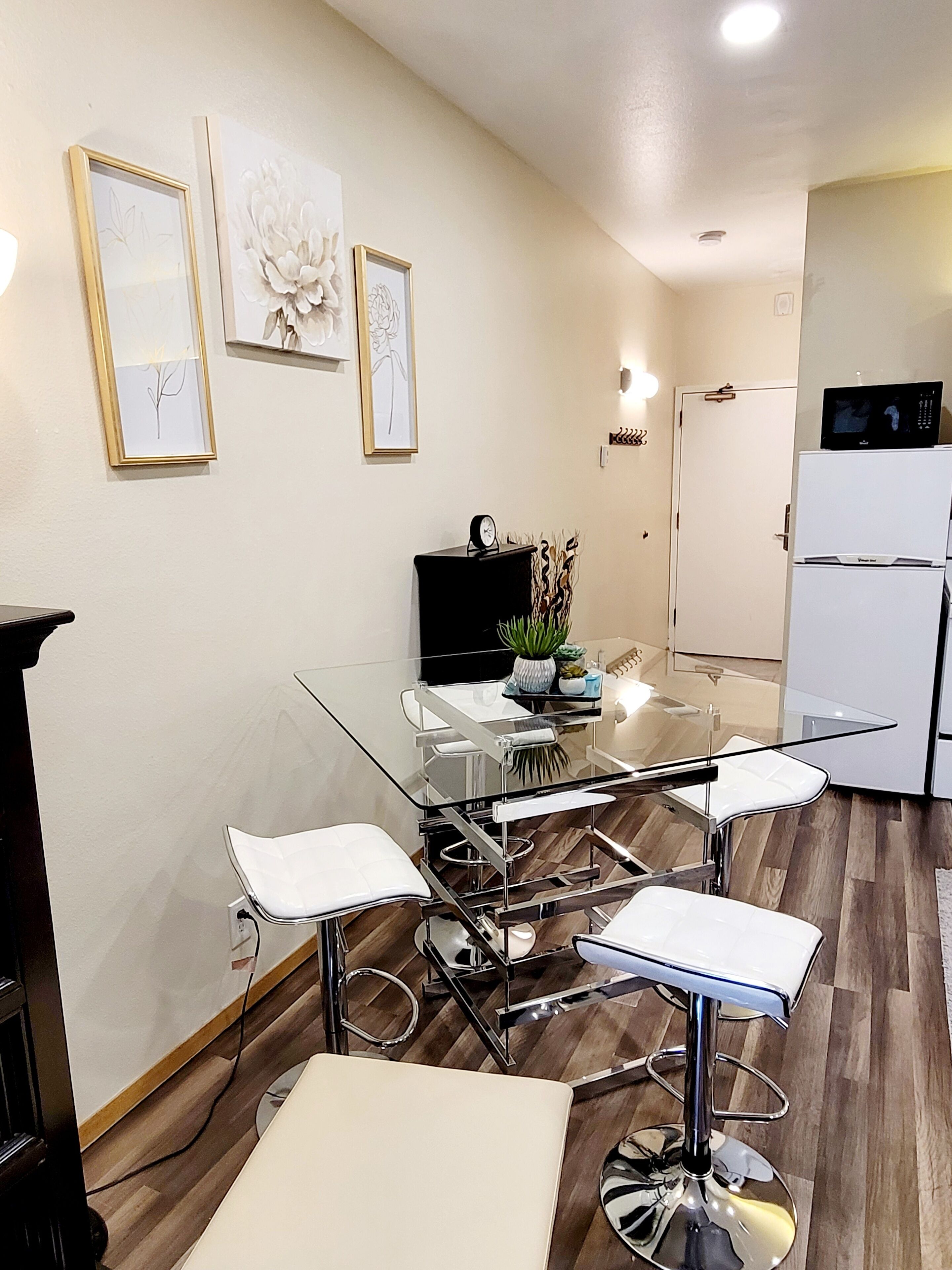 A modern kitchen with a white refrigerator, a microwave, and a dining area with a glass table and white chairs.