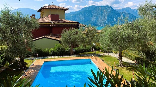 A pool surrounded by greenery and a mountain backdrop. - PELER Beth's House (Brenzone sul Garda)
